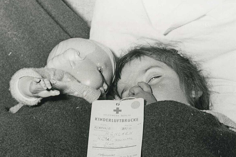 "Aktion Kinderluftbrücke": ein schlafendes Kind mit seiner Puppe während der Reise nach Westdeutschland (Paul Wittig / DRK)