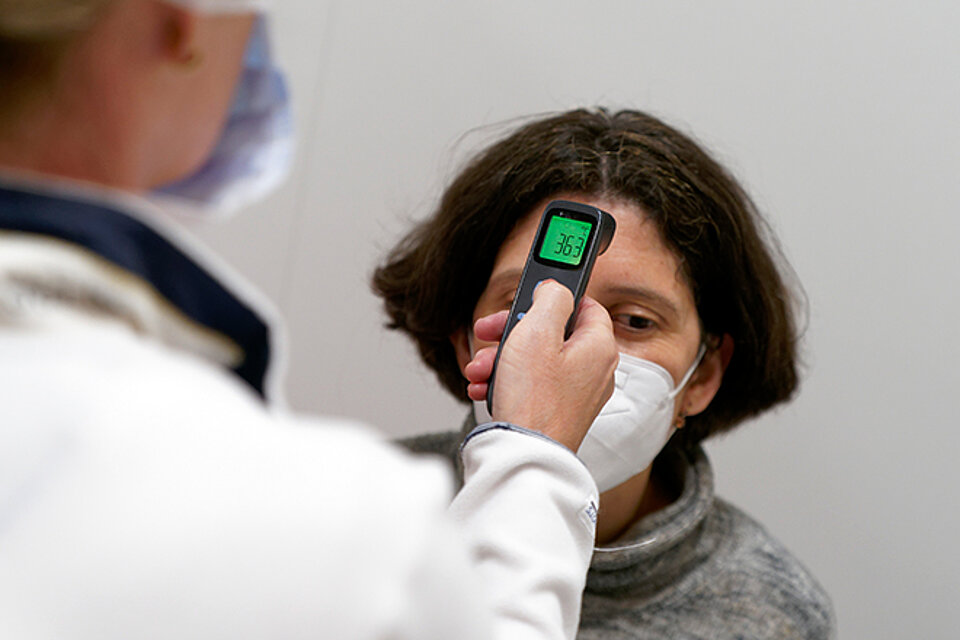 Medizinische Fachkraft misst Temperatur an Stirn einer Frau
