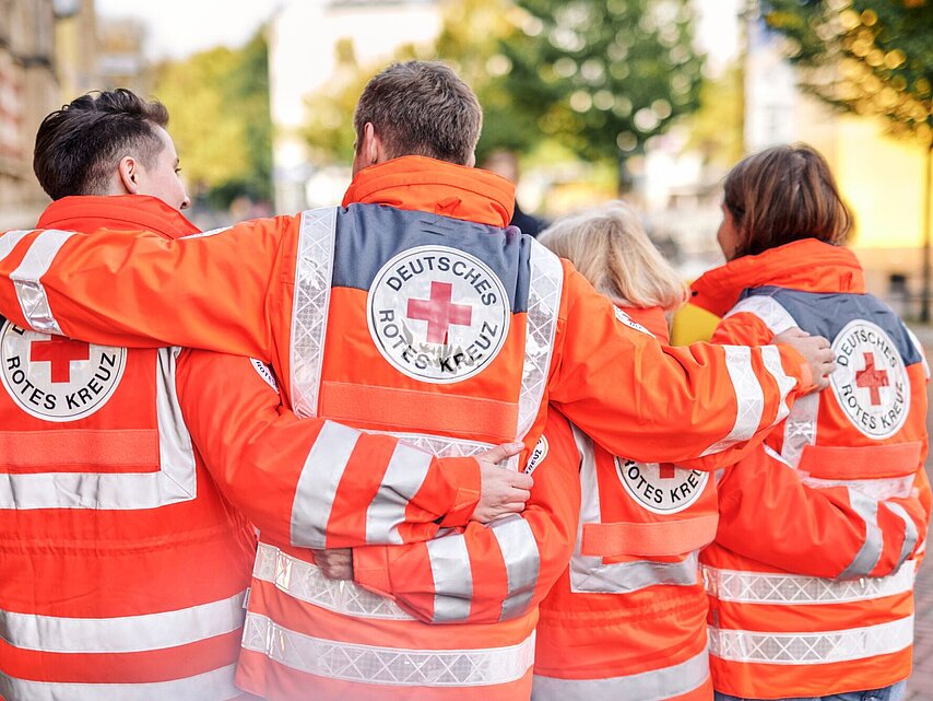 Symbolfoto drei DRK - Einsatzkräfte mit Rettungsdienstjacken mit DRK - Logo auf dem Rücken - 2021