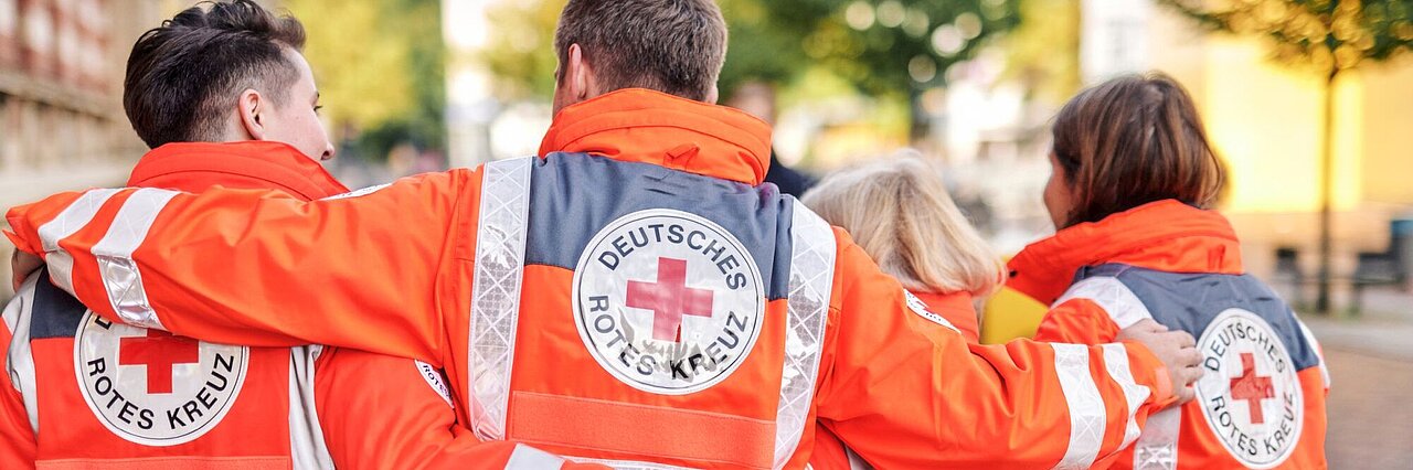 Symbolfoto drei DRK - Einsatzkräfte mit Rettungsdienstjacken mit DRK - Logo auf dem Rücken - 2021