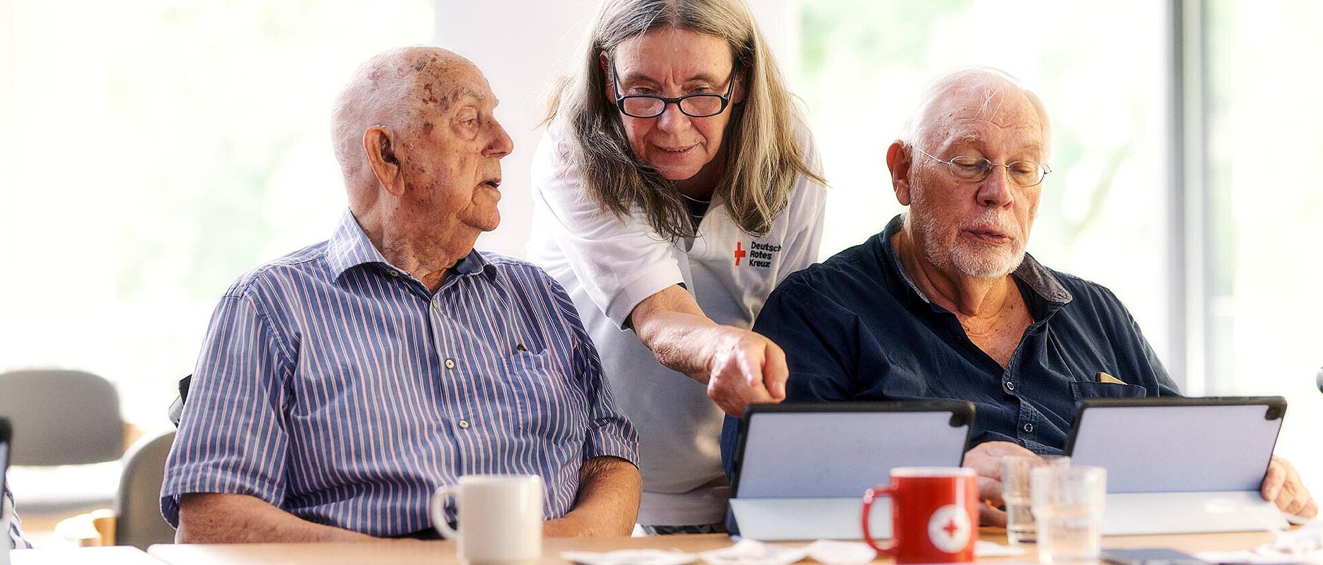 DRKlerin und Senioren schauen auf Tablets