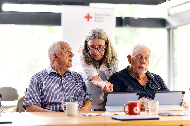 DRKlerin und Senioren schauen auf Tablets