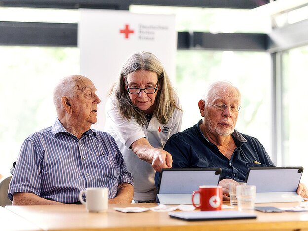 DRKlerin und Senioren schauen auf Tablets