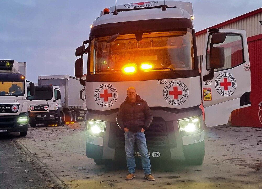 Vor mehreren großen LKWs des IKRK steht der Fahrer