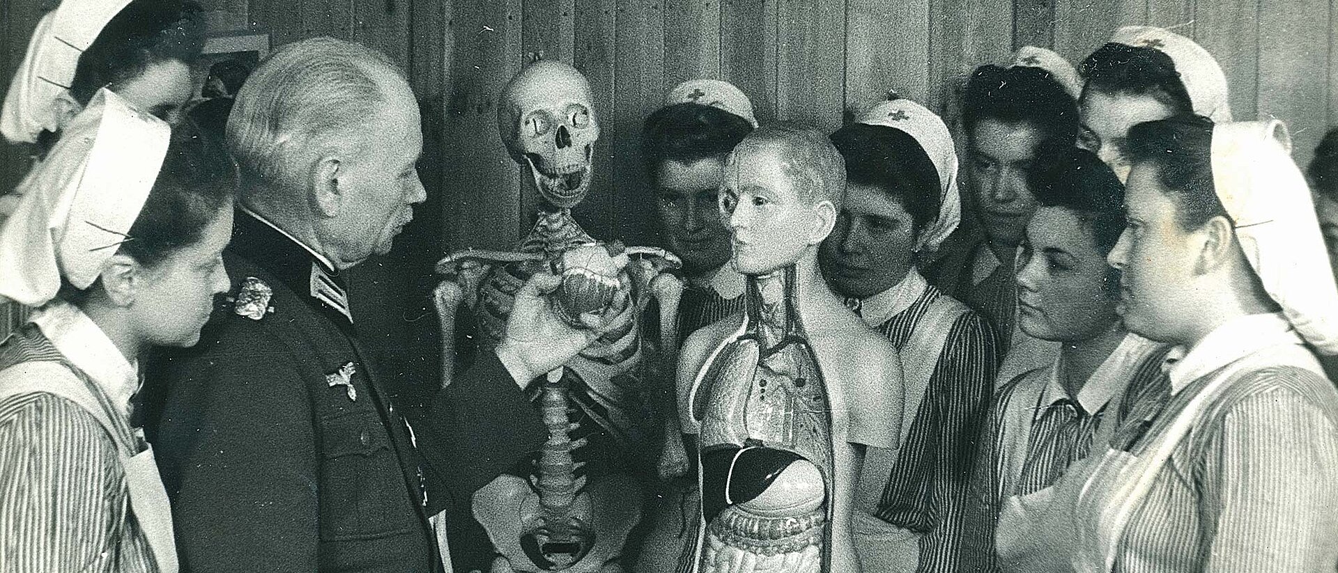 DRK-Schwesternhelferinnen und Arzt um ein Anatomiemodell