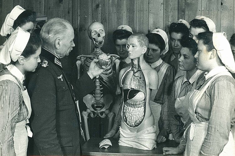 DRK-Schwesternhelferinnen und Arzt um ein Anatomiemodell