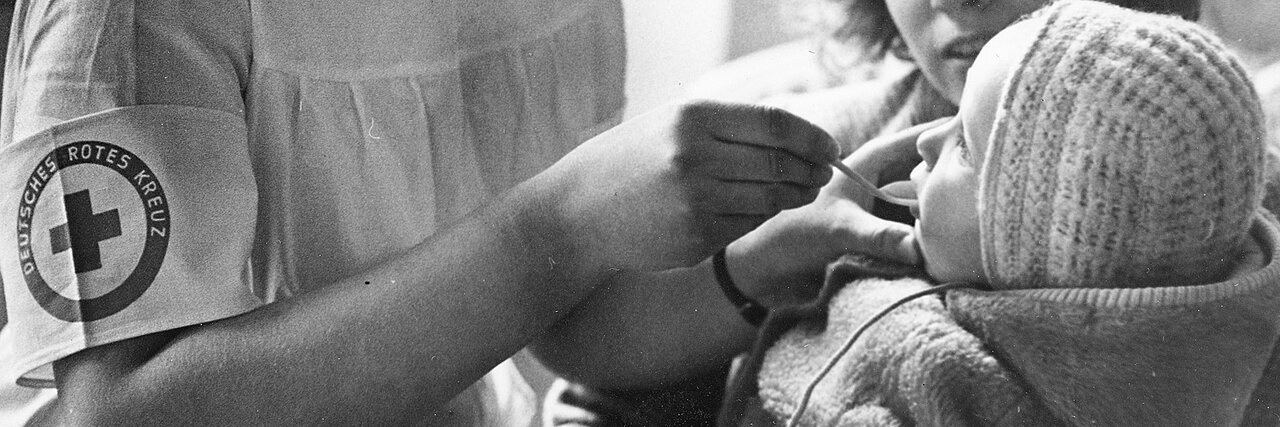 historisches Foto: Rotkreuzschwester verabreicht einem Baby Medizin