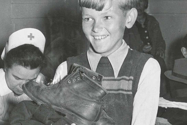 Ein Junge erhält Schuhe und Kleidung. Durch die Vermittlung des DRK spendete die Schwedische Hilfsorganisation Rädda Barnen ("Rettet die Kinder") zahlreiche Hilfsgüter (DRK)