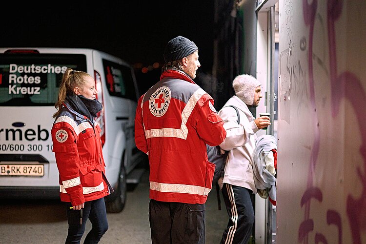 DRKler, DRKlerin und Mann an Tür einer Obdachlosenunterkunft