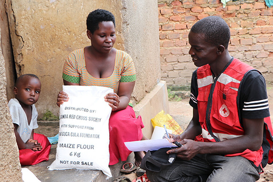 [Translate to Englisch:] Rotkreuzler überreicht Frau in Uganda Nahrung