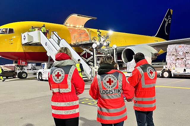 Drei DRK-Helfer vor Flugzeug