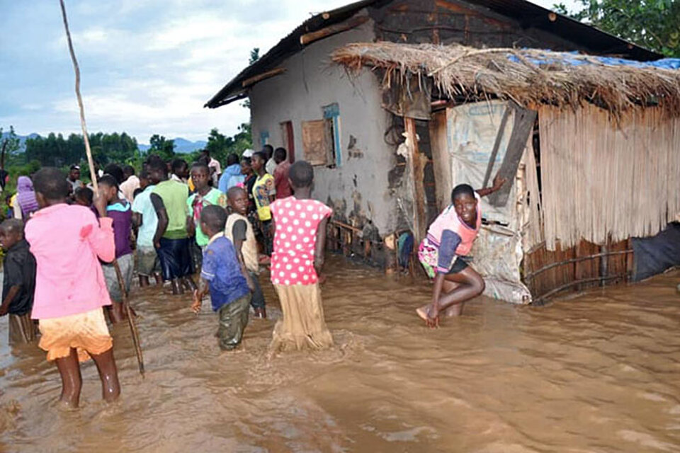 Foto: Menschen in Uganda vor einem Haus, Hochwasser steht ihnen bis zu den Knien.