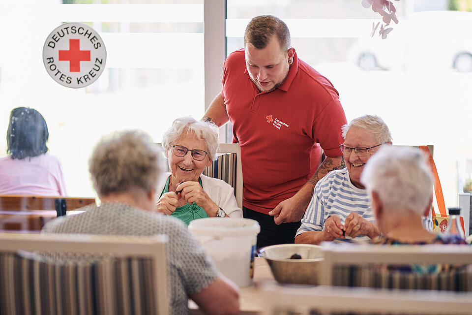 Pfleger zusammen mit pflegebedürftigen Menschen, die an einem Tisch essen und Obst entkernen.
