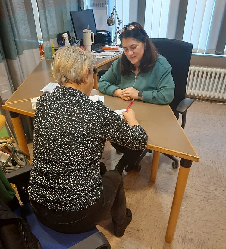Zwei Frauen sitzen in einem Raum an einem Tisch und sprechen miteinander,