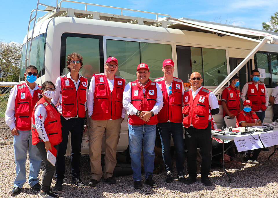 Mitarbeitende des DRK und des Honduranischen Roten Kreuzes stehen vor einem Bus, der ein humanitärer Servicepoint für Migranten ist. 