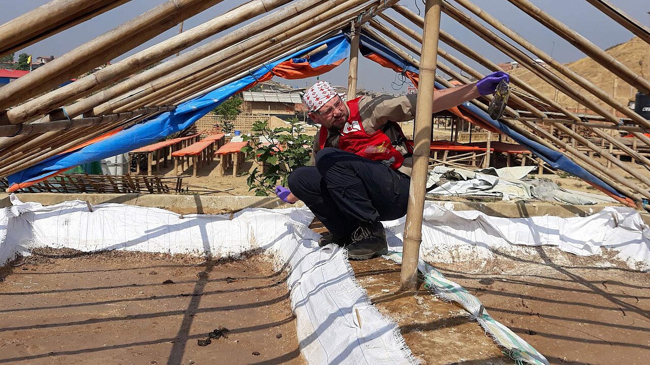 Ein Mann hockt im Lager Kutupalong unter einem Zelt und hält eine Abwasserprobe hoch