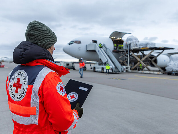 Person mit DRK Jacke vor einem Flugzeug