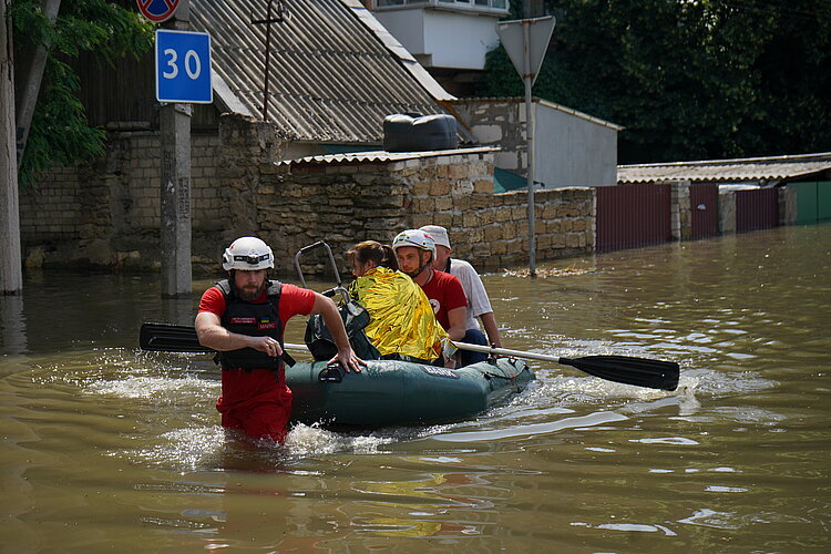 Helferinnen und Helfer des Ukrainischen Roten Kreuzes ziehen ein Boot durch das Hochwasser.