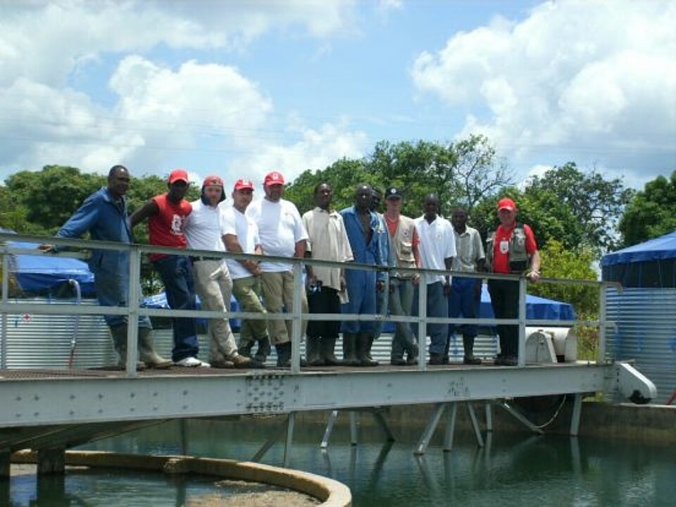 Foto: Ein Rotkreuz-Helferteam steht auf einer schmalen Brücke über einem Wassertank.