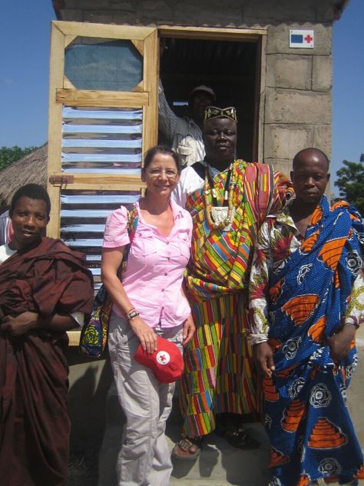 DRK-Mitarbeiterin mit Dorfvorstehern vor Latrine