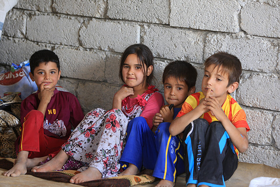 Vier irakische Kinder sitzen auf Boden an Steinwand