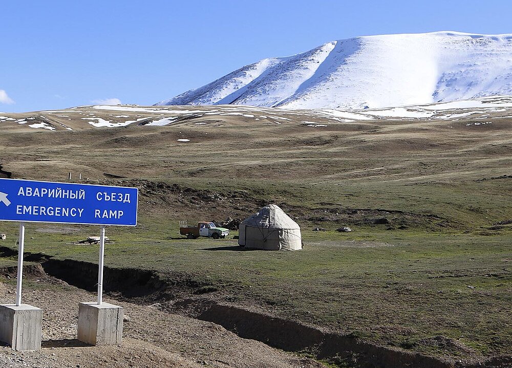 Wiese vor schneebedeckten Bergen und Sicherheitsrampen-Schild