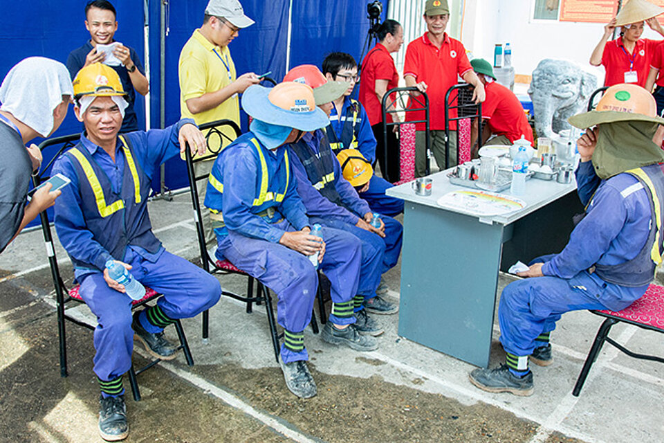 Vietnamesische Bauarbeiter mit Wasserflaschen in Erfrischungszelt