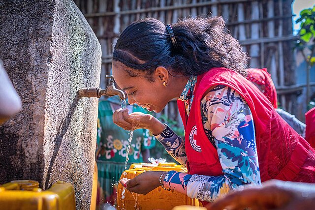 Freiwillige trinkt Wasser aus Hand am Brunnen