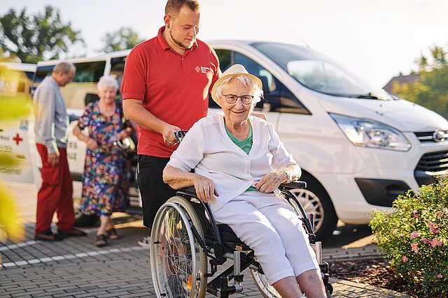 DRK-Pfleger und Seniorin im Rollstuhl vor DRK-Bus