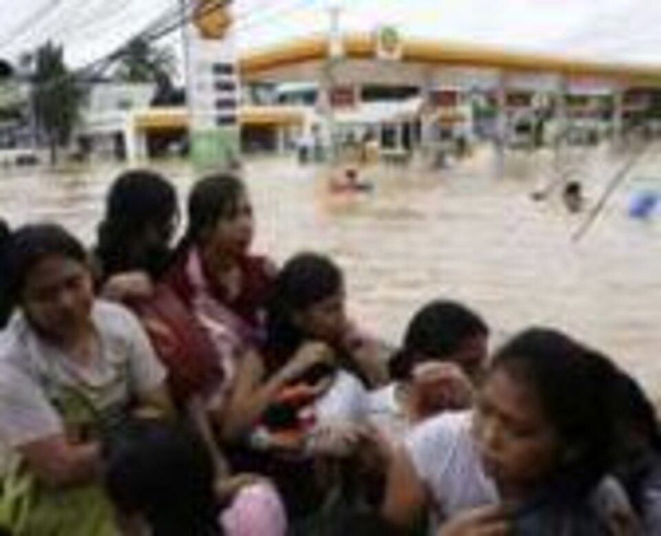 Foto: Philippinische Frauen und Kinder im Boot. Im Hintergrund überflutete Straße und Tankstelle.