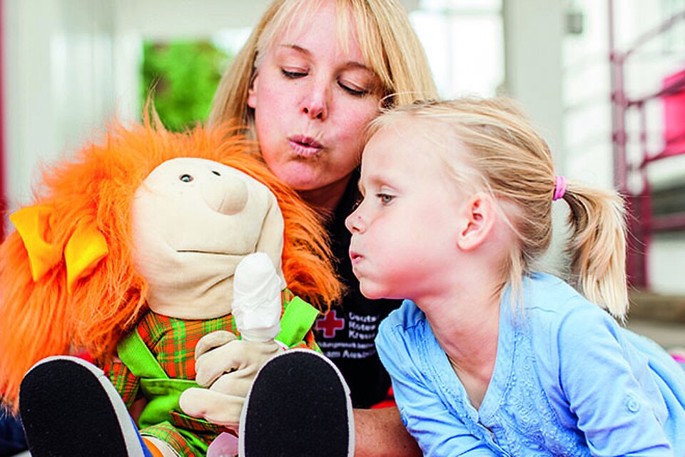 Foto: Kinder und ihre Erzieherin pusten den verbundenen Finger einer Puppe