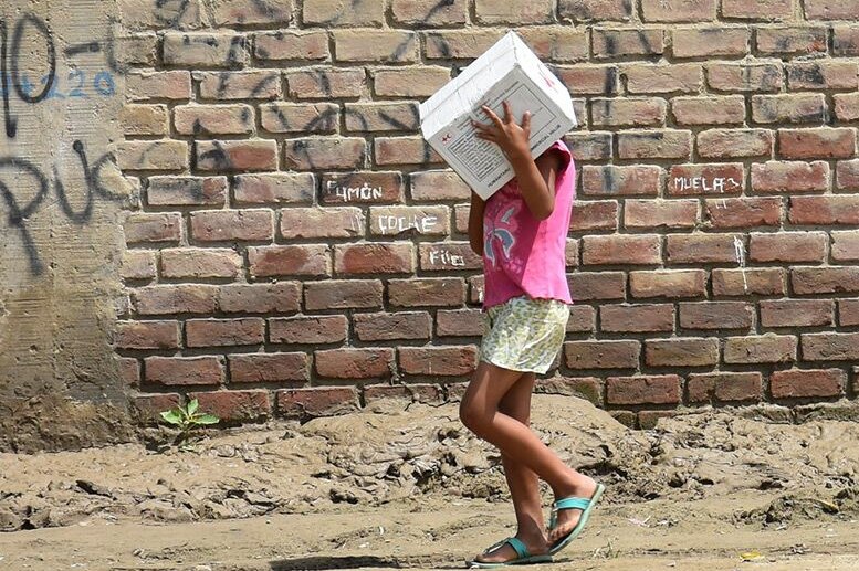 Peruanische Kinder tragen Hilfsgüter vor einer Mauer
