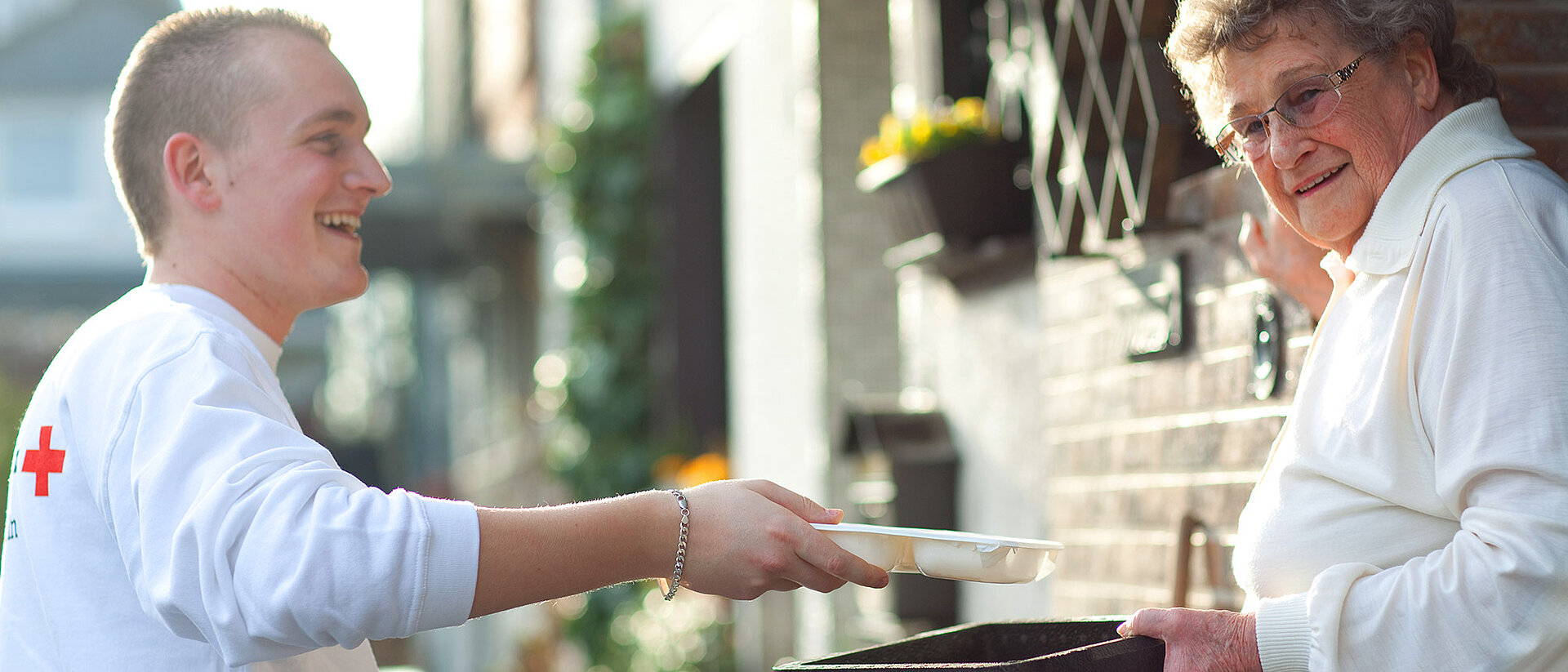 Menüservice DRKler übergibt Box an Seniorin