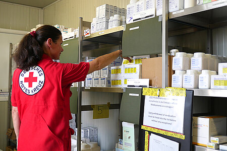 Eine DRK-Mitarbeiterin greift in ein Regal mit Medikamenten.