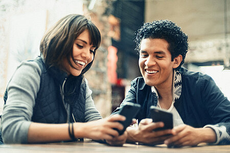 Foto: Mann und Frau im Gespräch - auf ihre Mobiltelefone schauend