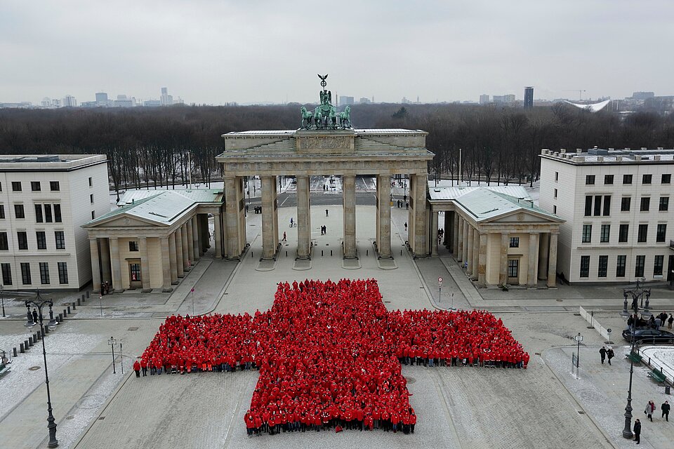 Helfende des DRK bilden vor dem Brandenburger Tor ein großes rotes Kreuz.