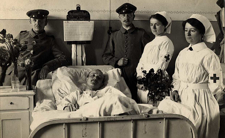Krankenschwestern und Soldaten am Krankenbett eines Verwundeten (DRK)