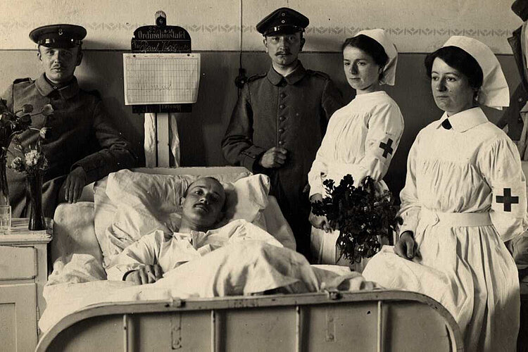 Krankenschwestern und Soldaten am Krankenbett eines Verwundeten (DRK)