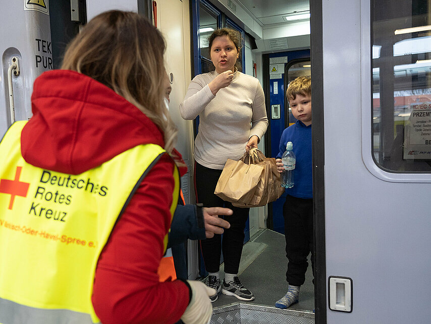 DRKlerin spricht mit zwei ukrainischen Kindern im Zug