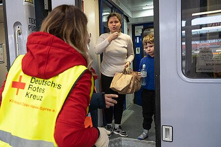 DRKlerin spricht mit zwei ukrainischen Kindern im Zug