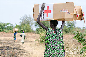 Südsudanesin trägt ein Rotkreuz-Hilfsgüterpaket