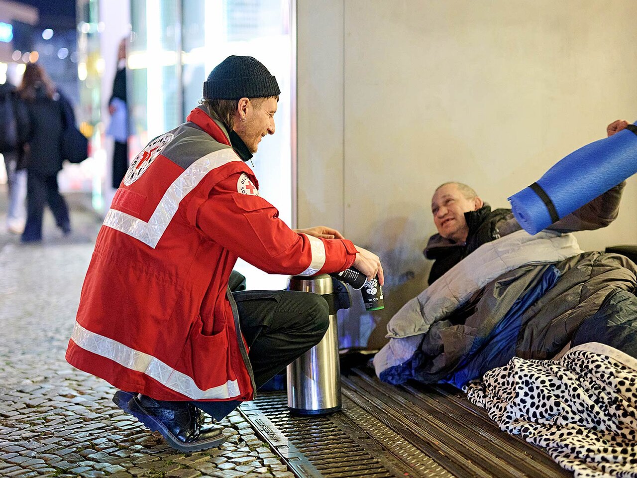 DRKler gibt Kaffee und Isomatte an Obdachlosen