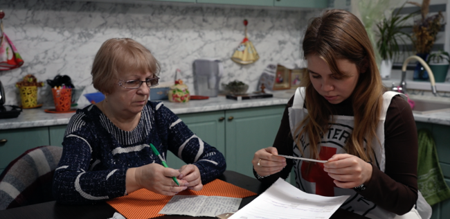 Zwei Frauen sitzen an einem Küchentisch und schauen Briefe an.