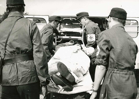 Rettungseinsatz bei einem Unfall: Sanitäter tragen einen Verletzten in einen Krankenwagen, sechziger Jahre (Willy Heudtlass / DRK)