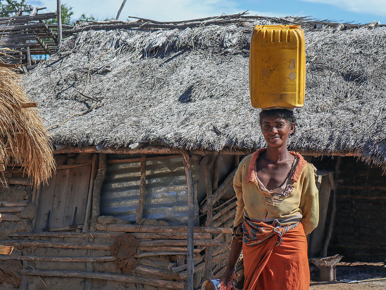 Madagassin mit Wasserkanister auf Kopf vor Hütte