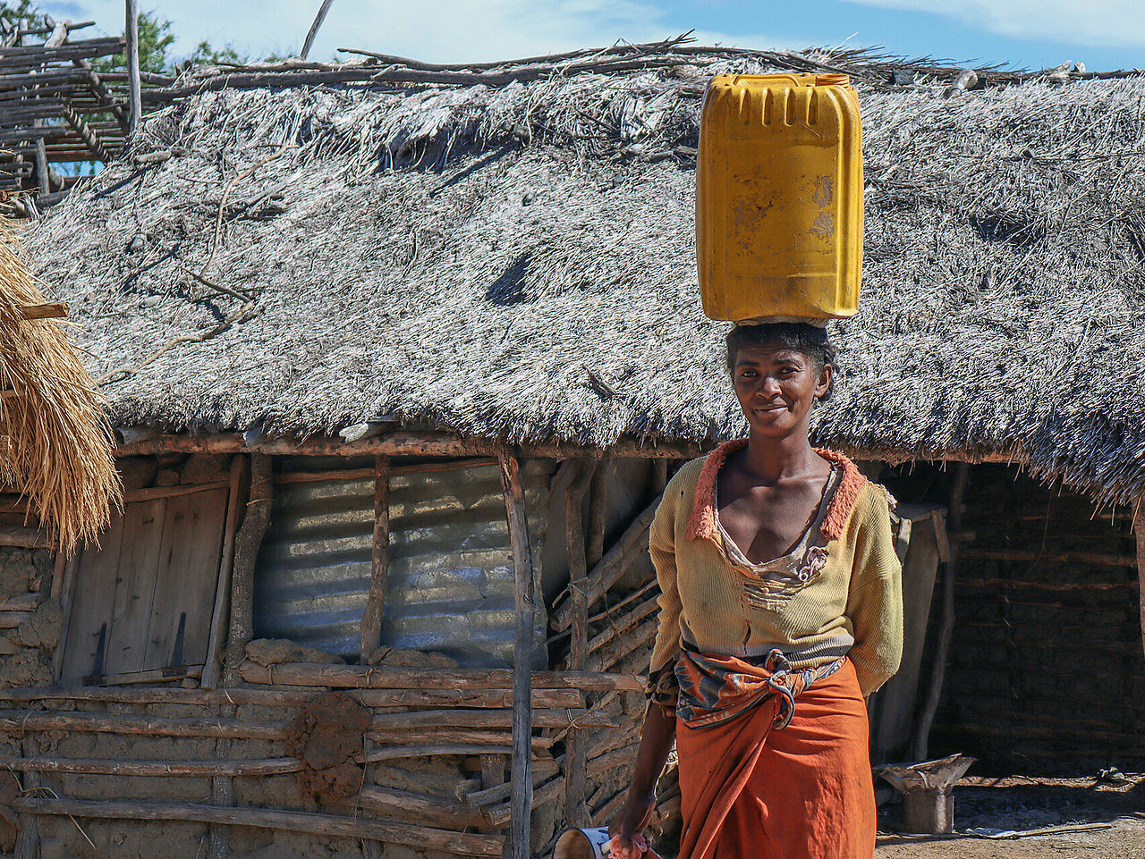 Madagassin mit Wasserkanister auf Kopf vor Hütte