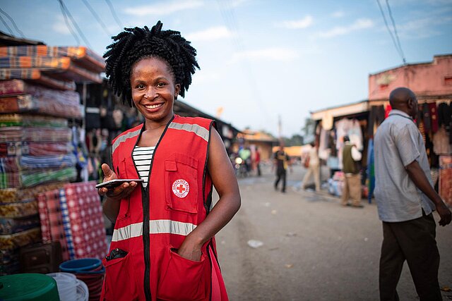 Ugandische Rotkreuz-Mitarbeiterin auf Markt mit Handy