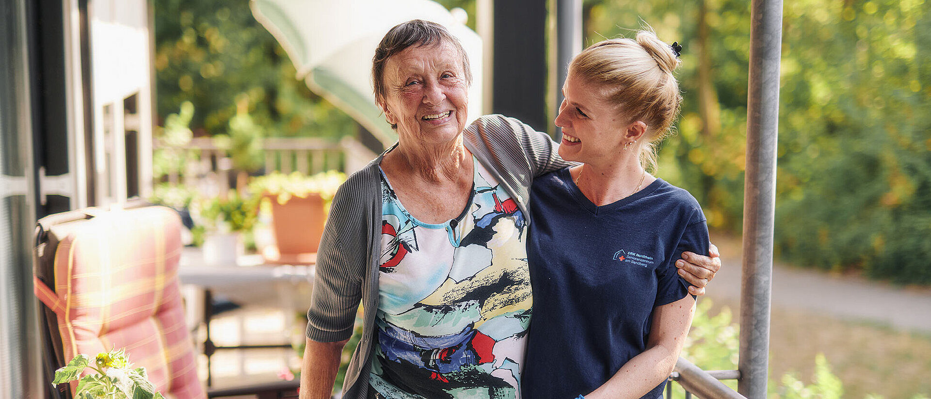Seniorin lacht mit DRKlerin auf Balkon