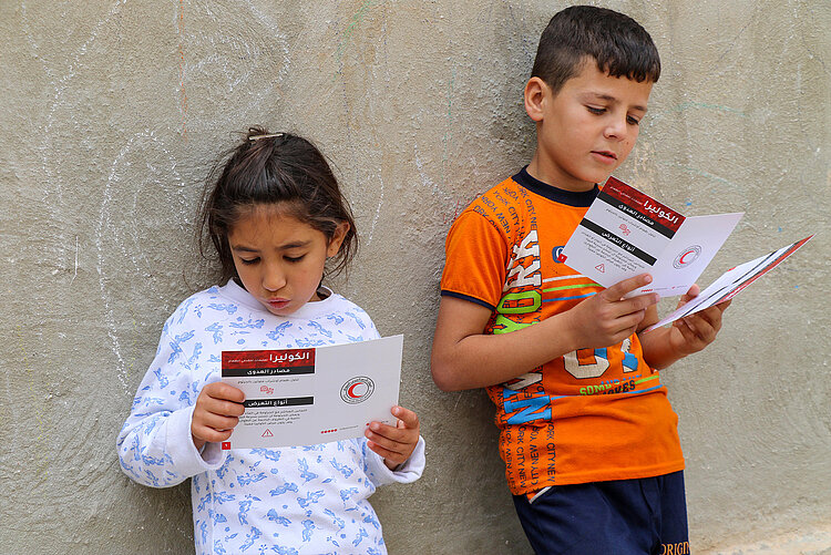 Zwei Kinder in Syrien lesen eine Broschüre zur Aufklärung über Cholera