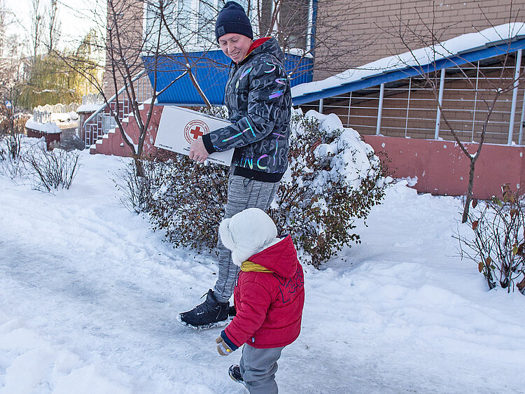 Mann und Kind mit Rotkreuz-Paket in der Ukraine 